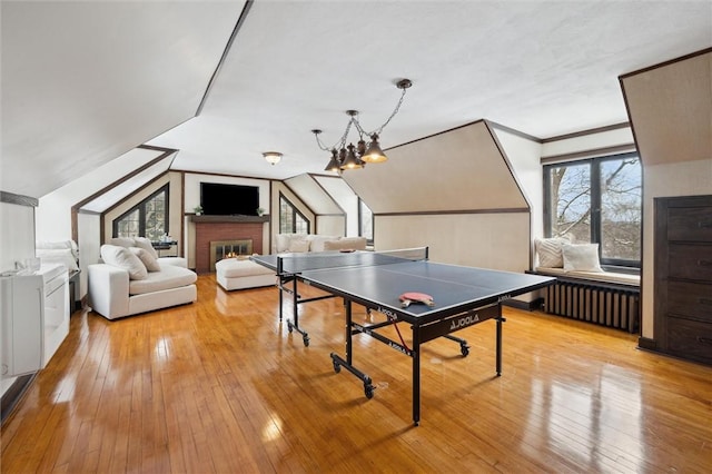 game room with radiator heating unit, vaulted ceiling, crown molding, light wood-type flooring, and a brick fireplace