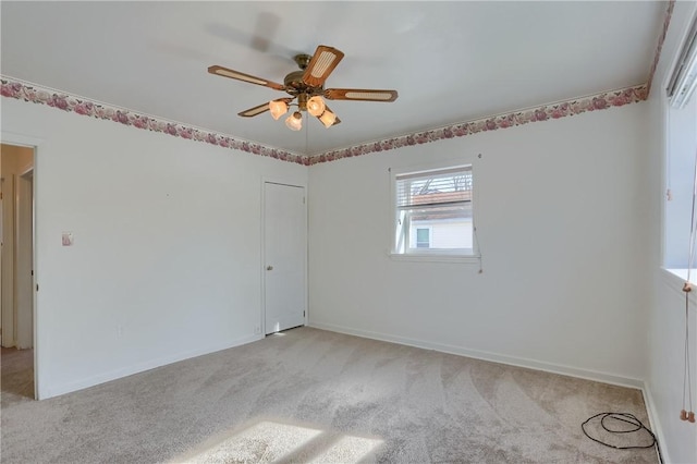 spare room with a ceiling fan, light colored carpet, and baseboards