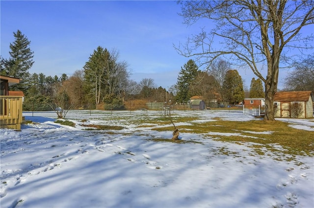 yard layered in snow featuring a shed, an outdoor structure, and fence