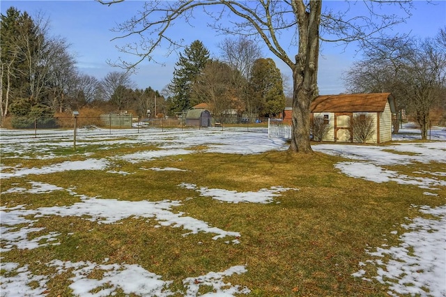 yard layered in snow featuring a storage unit, an outdoor structure, fence, and a detached carport