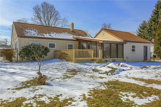 snow covered rear of property with a chimney and a sunroom