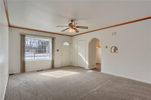 spare room with light carpet, baseboards, arched walkways, ceiling fan, and crown molding