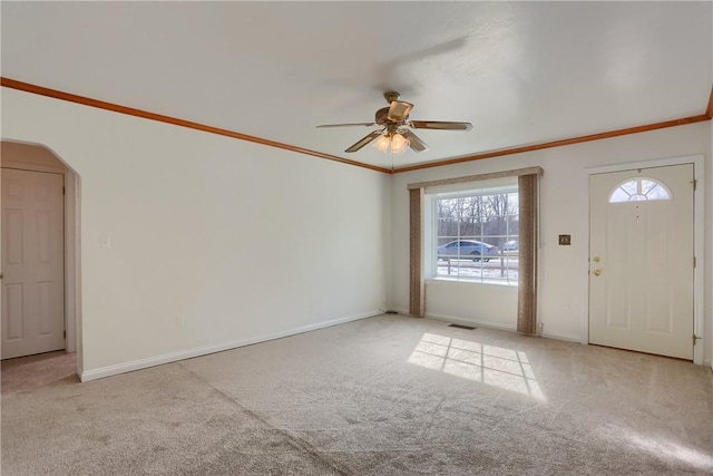 entryway with arched walkways, light colored carpet, a ceiling fan, baseboards, and ornamental molding