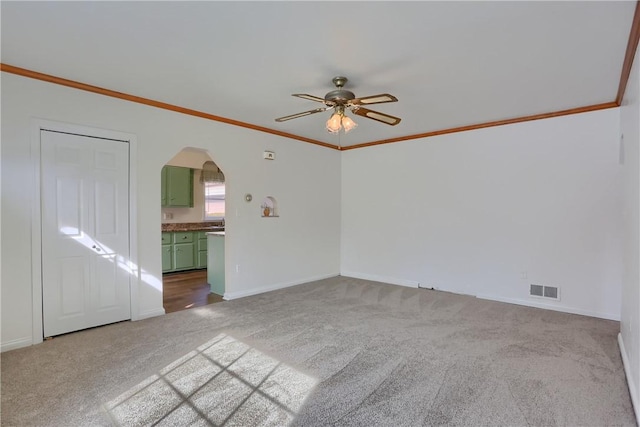 unfurnished living room with arched walkways, carpet, visible vents, ornamental molding, and a ceiling fan