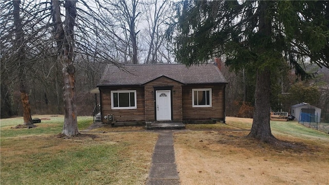 view of front of property with an outbuilding, roof with shingles, a shed, a chimney, and a front yard