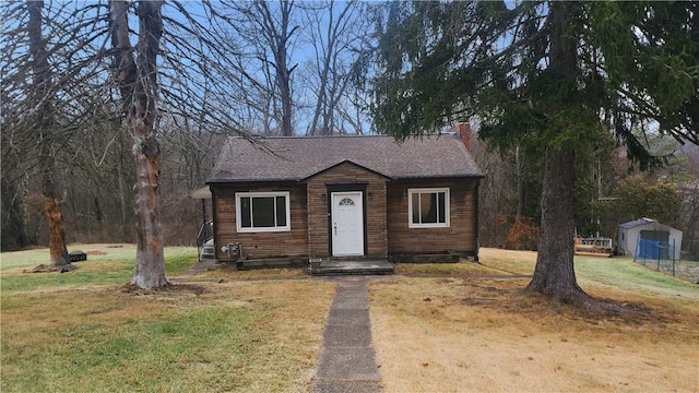 bungalow-style home with a shingled roof, a chimney, and a front lawn