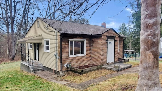 view of front of property with roof with shingles, a front lawn, and a chimney