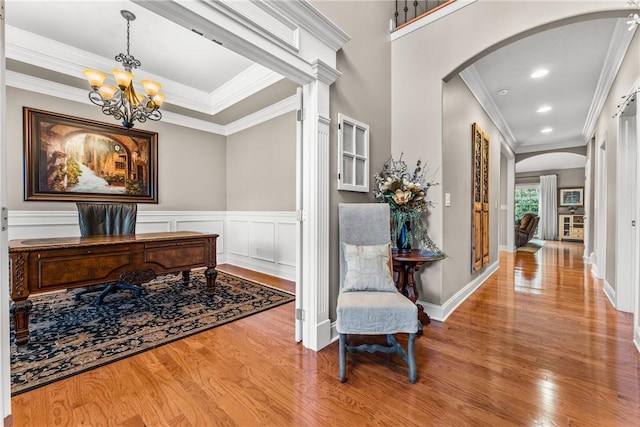 corridor with arched walkways, a notable chandelier, crown molding, light wood finished floors, and a decorative wall