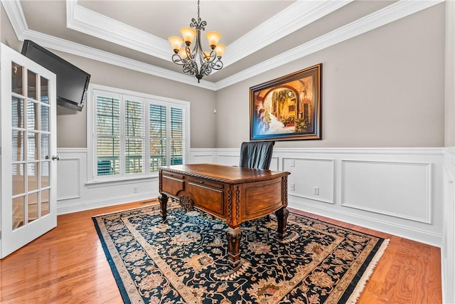 office featuring a decorative wall, wood finished floors, ornamental molding, a raised ceiling, and an inviting chandelier