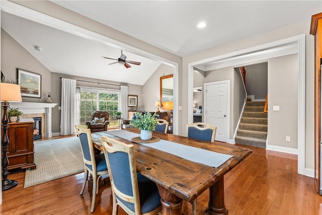 dining area with stairs, vaulted ceiling, a glass covered fireplace, and light wood-style floors