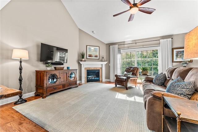 living room with a ceiling fan, a glass covered fireplace, wood finished floors, high vaulted ceiling, and baseboards