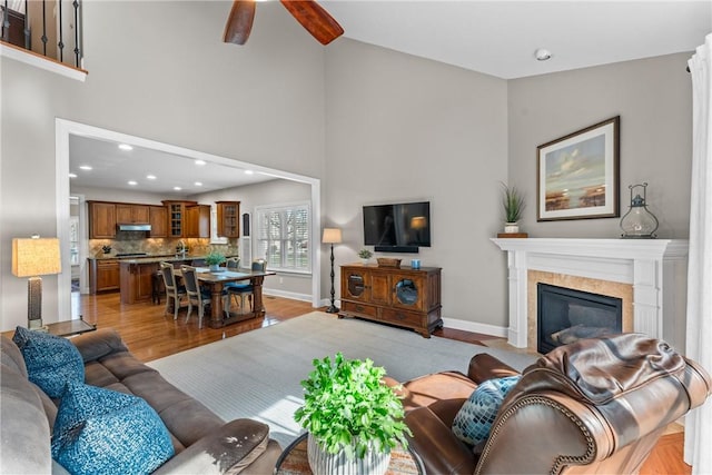 living room featuring a fireplace with flush hearth, ceiling fan, high vaulted ceiling, light wood-type flooring, and baseboards