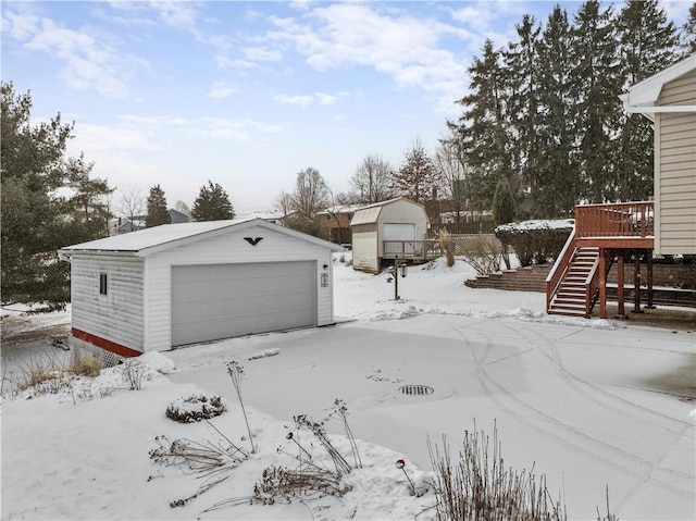 snowy yard featuring an outbuilding, a deck, a detached garage, and stairs