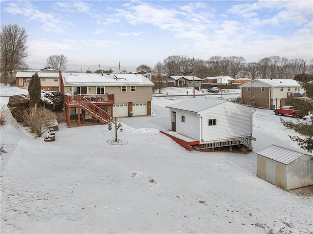 snow covered house featuring stairs, a deck, an attached garage, and a residential view