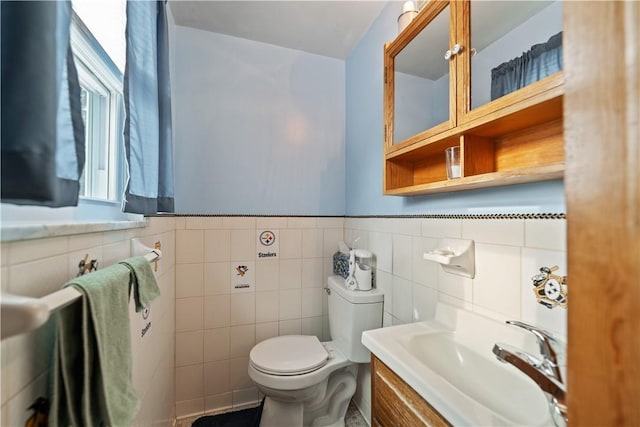 half bathroom featuring tile walls, a wainscoted wall, vanity, and toilet