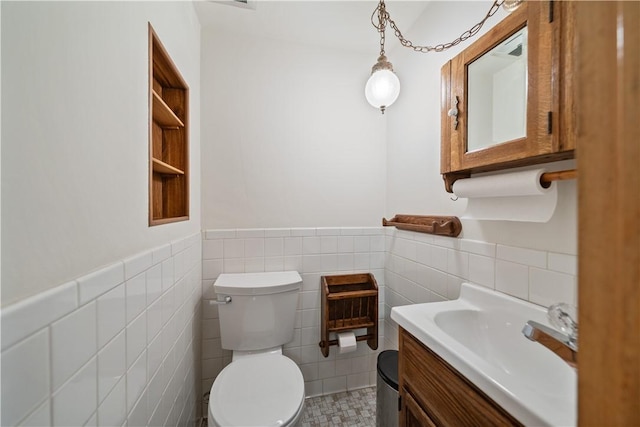 half bath featuring toilet, wainscoting, vanity, and tile walls