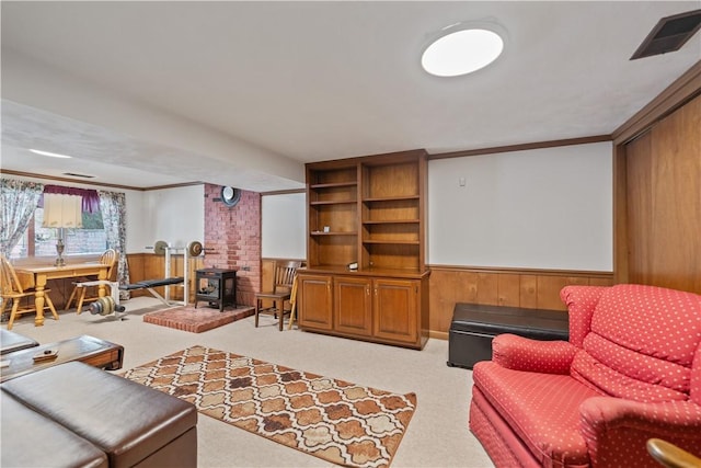 living area featuring a wainscoted wall, visible vents, ornamental molding, a wood stove, and light carpet