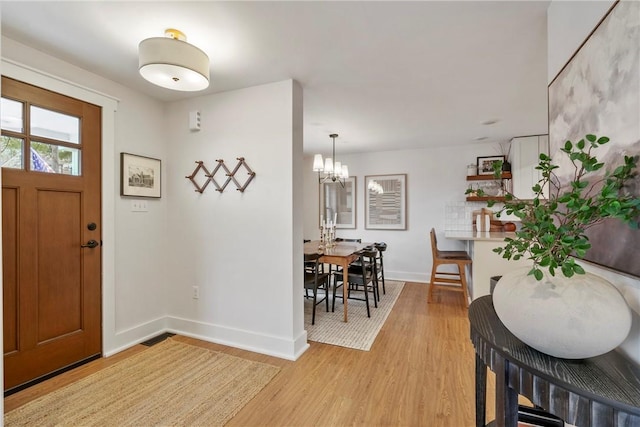 foyer entrance featuring a notable chandelier, light wood-type flooring, and baseboards