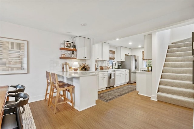 kitchen featuring a breakfast bar area, stainless steel appliances, white cabinets, light countertops, and open shelves