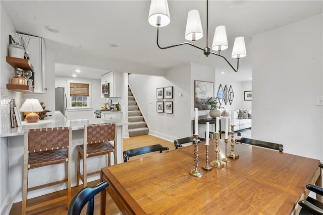 dining space featuring light wood finished floors, recessed lighting, a chandelier, baseboards, and stairs