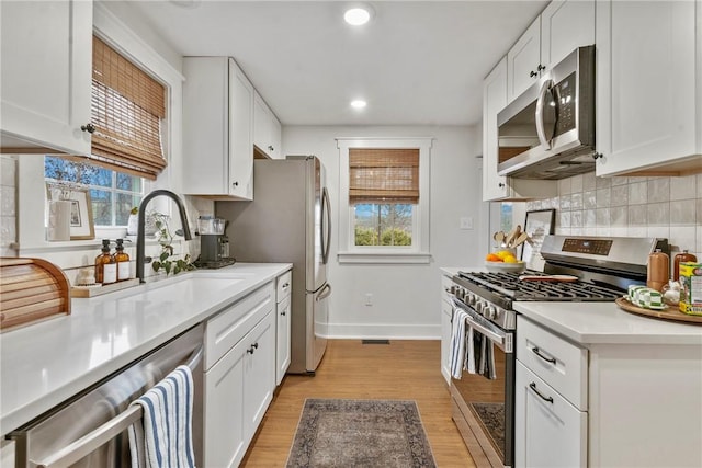 kitchen with white cabinets, decorative backsplash, stainless steel appliances, light countertops, and a wealth of natural light