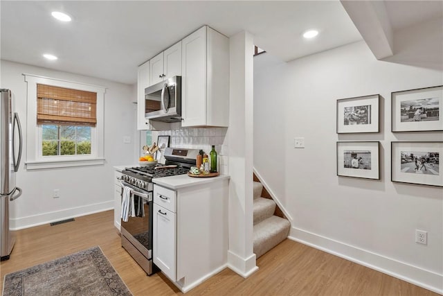 kitchen featuring visible vents, decorative backsplash, stainless steel appliances, light countertops, and white cabinetry