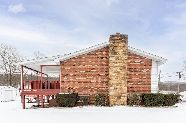 view of snowy exterior with a chimney and brick siding