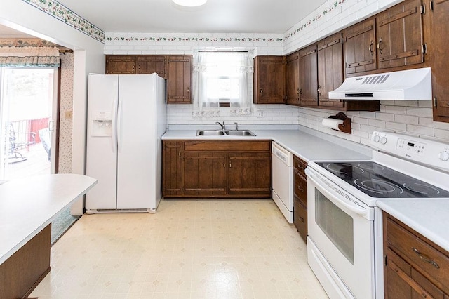 kitchen with under cabinet range hood, white appliances, a sink, light countertops, and light floors