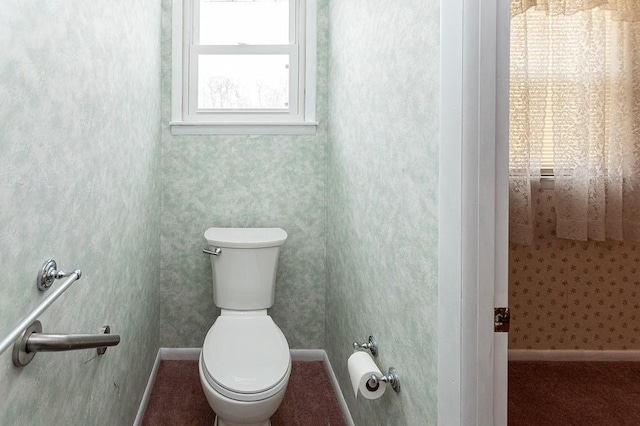 bathroom featuring toilet, wallpapered walls, and baseboards