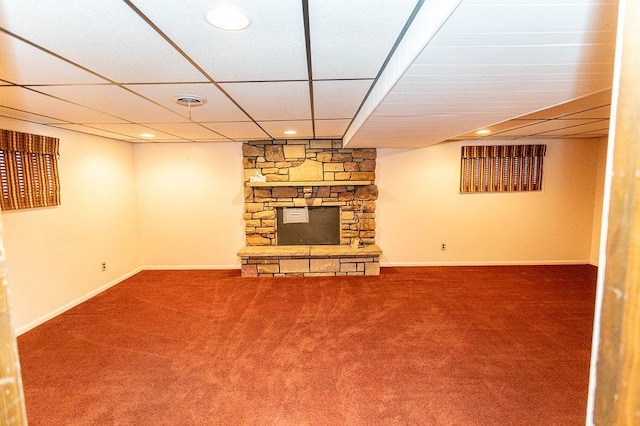 finished basement with baseboards, carpet flooring, a stone fireplace, and a drop ceiling