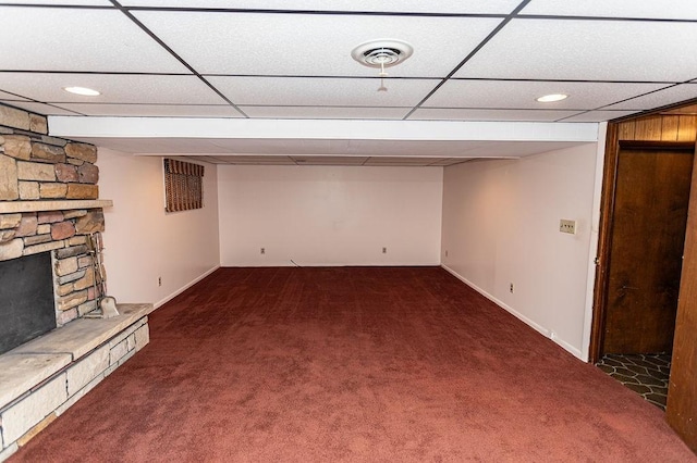 finished basement with a paneled ceiling, dark carpet, a fireplace, and visible vents