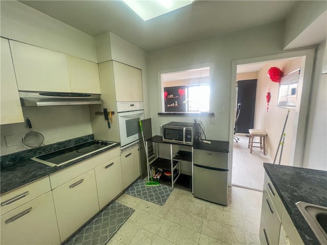 kitchen with under cabinet range hood, stainless steel microwave, stovetop, and white oven