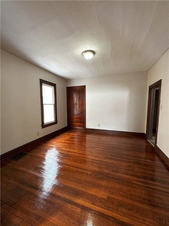 spare room featuring dark wood-style floors, visible vents, and baseboards