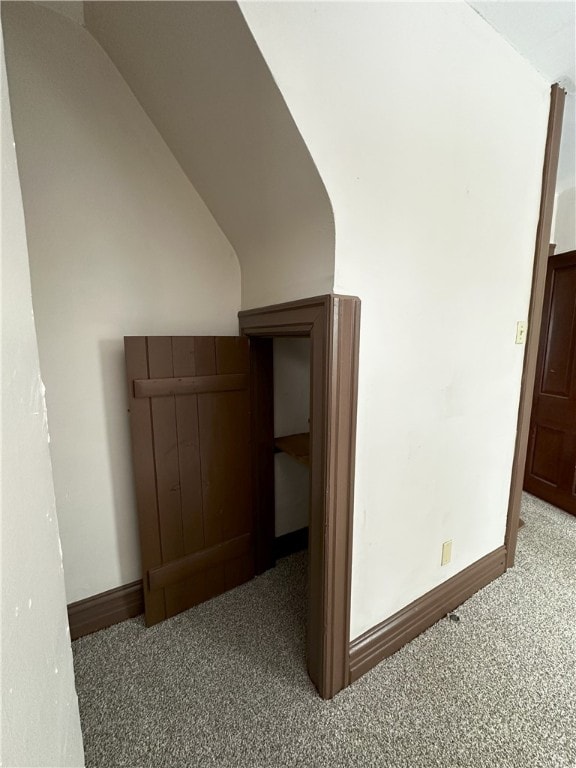 hallway featuring carpet floors, baseboards, and lofted ceiling