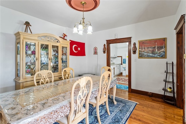 dining area with light wood-style flooring, baseboards, and a notable chandelier