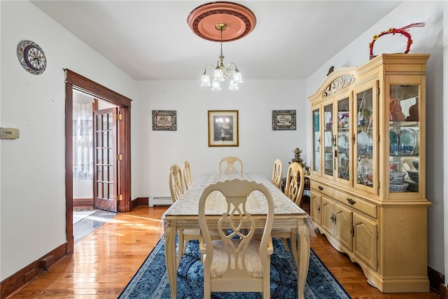 dining space with light wood-style floors, a baseboard radiator, baseboards, and an inviting chandelier