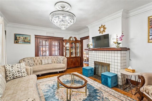 living room featuring a notable chandelier, a fireplace, wood finished floors, and crown molding