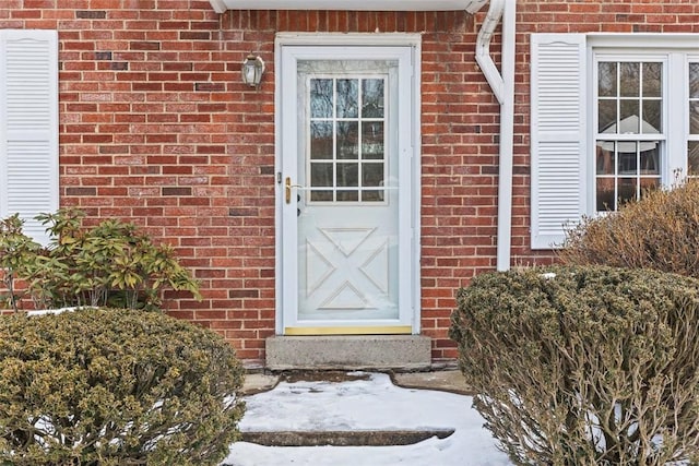 snow covered property entrance with brick siding