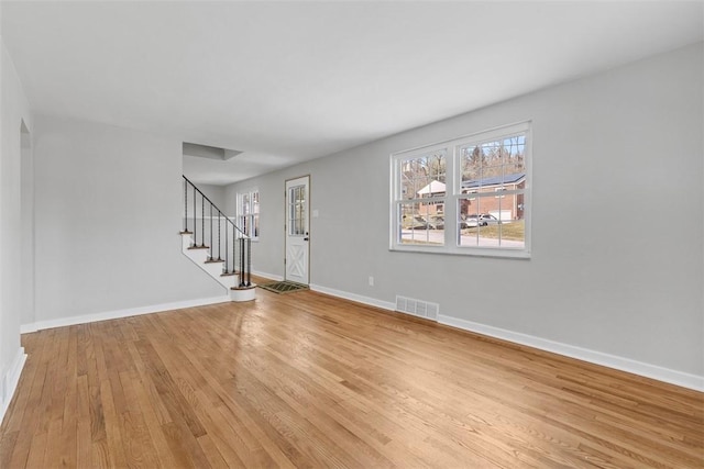 unfurnished living room with stairway, light wood-style flooring, visible vents, and baseboards