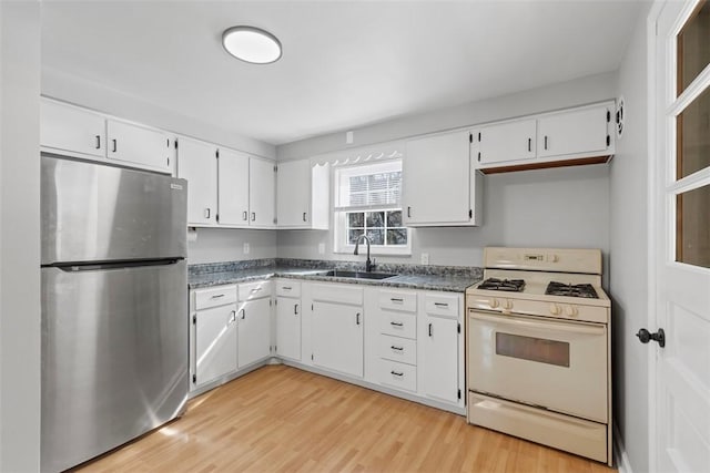 kitchen with a sink, white cabinetry, white range with gas cooktop, freestanding refrigerator, and dark countertops