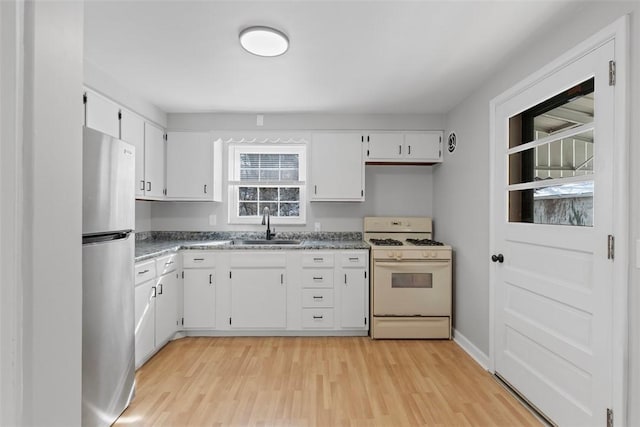 kitchen with white cabinets, dark countertops, freestanding refrigerator, white gas range, and a sink