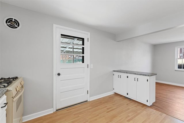 kitchen with light wood-style flooring, white cabinetry, baseboards, white gas range oven, and dark countertops