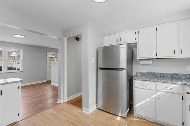 kitchen with freestanding refrigerator, baseboards, white cabinetry, and light wood finished floors