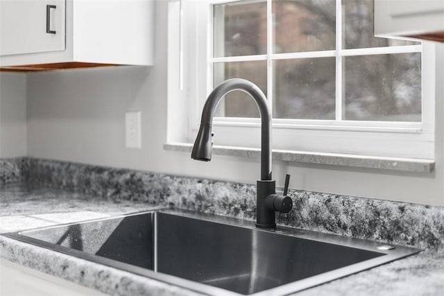 interior details with light stone counters, a sink, and white cabinets