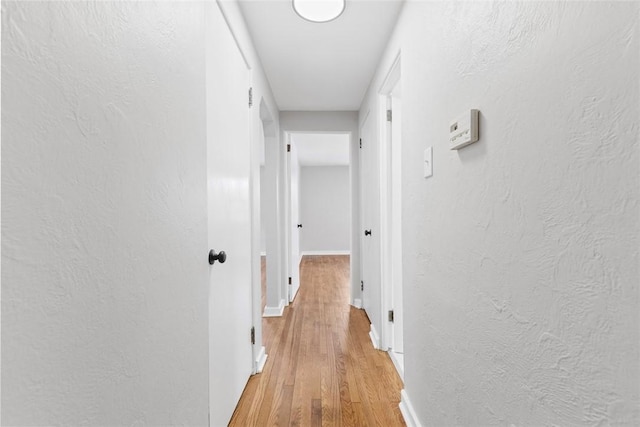 corridor with baseboards, wood finished floors, and a textured wall