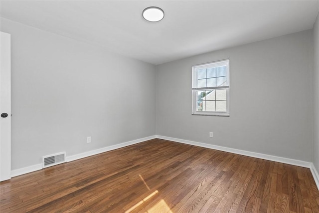 empty room featuring wood finished floors, visible vents, and baseboards