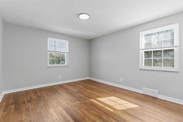 spare room with wood finished floors, visible vents, and baseboards