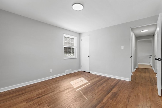 unfurnished room featuring visible vents, baseboards, and wood finished floors