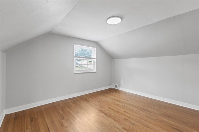 additional living space featuring lofted ceiling, visible vents, baseboards, and wood finished floors