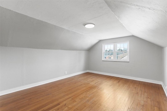 additional living space with a textured ceiling, baseboards, vaulted ceiling, and wood finished floors